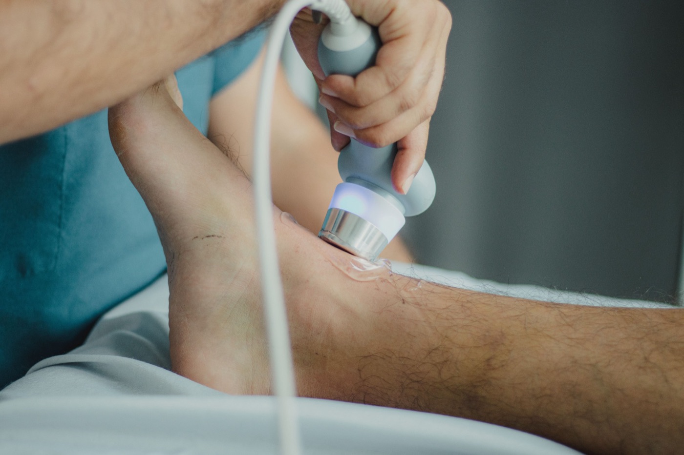 A practitioner applying a shockwave therapy applicator to a client's ankle